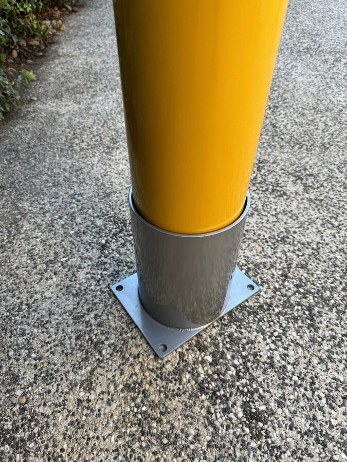 Removable safety bollard parked in a bolt-down storage holder on a concrete path